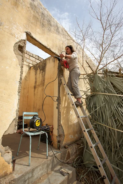 Vrouw werken en staande op een ladder met een driller — Stockfoto