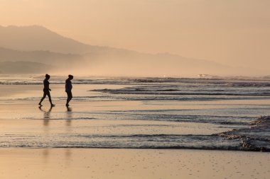 Silhouette of two people walking on the beach with beutuful ligh clipart