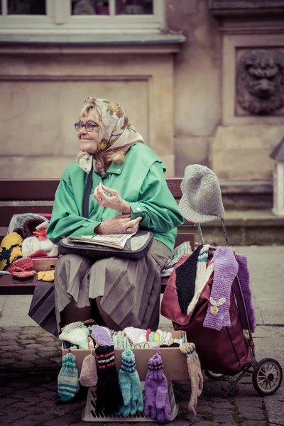 Old woman sitting on a bench and selling gloves — Stock Photo, Image