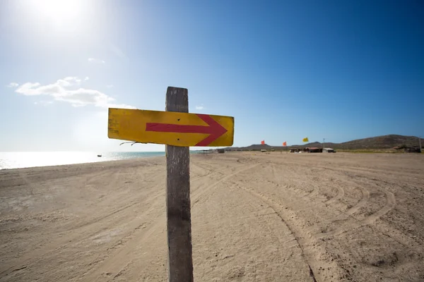 Wooden sign with an arrow and the beach in the backgound — Stock Photo, Image