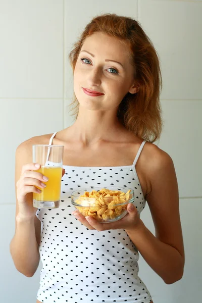 Femme tenant verre avec du jus d'orange et bol avec des flocons de maïs — Photo