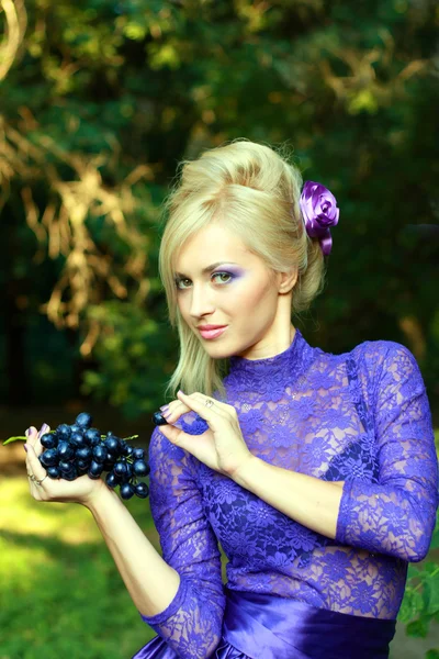 Vrouw in violet mode jurk eten druif — Stockfoto
