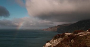Gökkuşağı ve hareket eden bulut oluşumları, Slieve Ligi, Donegal, İrlanda Atlantik Okyanusu kıyılarındaki kayalıkların fırtınalı durumdaki 4K zaman dilimi videosu