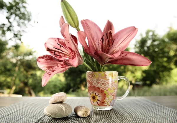 Fresh lilies in a glass of water on garden background — Stock Photo, Image