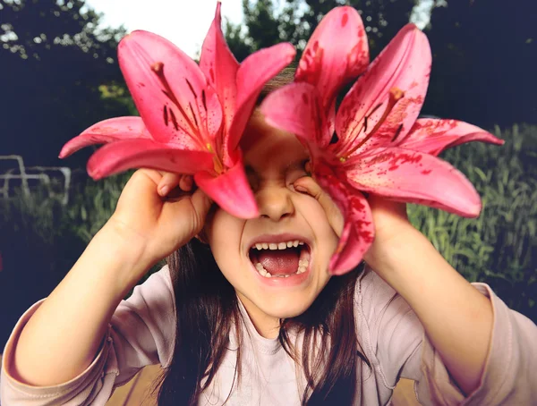 Glad flicka som leker med blommor, tittar in i kameran genom Lilja — Stockfoto