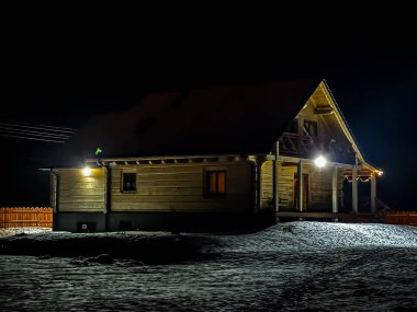 Bir kış akşamı, hafif karla kaplı bir bina arazisinde bir ahşap ev.