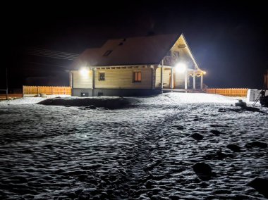 Bir kış akşamı, hafif karla kaplı bir bina arazisinde bir ahşap ev.