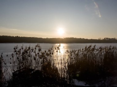 Kışın gölün buzla kaplı yüzeyinde gün batımı