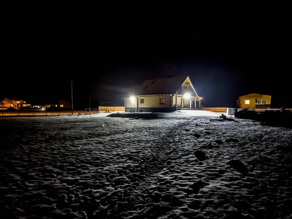 Bir kış akşamı, hafif karla kaplı bir bina arazisinde bir ahşap ev.