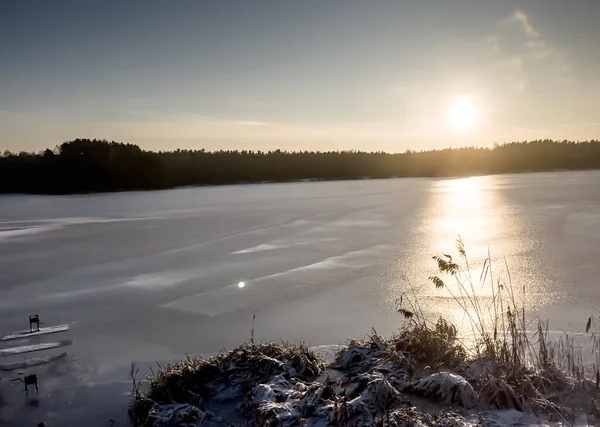 Kışın gölün buzla kaplı yüzeyinde gün batımı