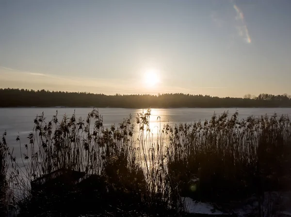 Kışın gölün buzla kaplı yüzeyinde gün batımı