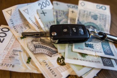 Polonya zloti banknotlarının üzerinde duran bir araba anahtarı. Benzin fiyatlarındaki artış, arabanın kullanımına bağlı olarak daha yüksek harcamalara yol açtı.