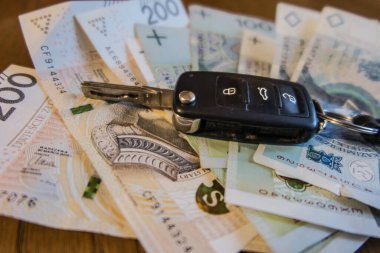 Polonya zloti banknotlarının üzerinde duran bir araba anahtarı. Benzin fiyatlarındaki artış, arabanın kullanımına bağlı olarak daha yüksek harcamalara yol açtı.