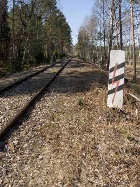 Demiryolu hattı ormandan geçiyor. Sembolün ilerisinde ve elektrikli raylara giriş uyarısı var..