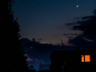 Orak şeklinde bir ay kısmen bulutlu bir akşam gökyüzünde yükseliyor.