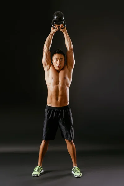 Asian man lifting a kettlebell over his head — Stock Photo, Image
