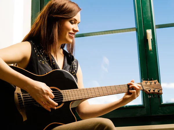 Усміхнена жінка грає на гітарі біля вікна — стокове фото
