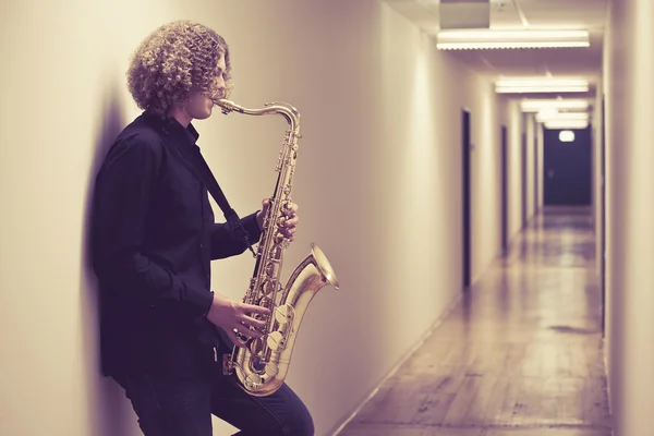 Man playing the saxophone in a hallway — Stock Photo, Image