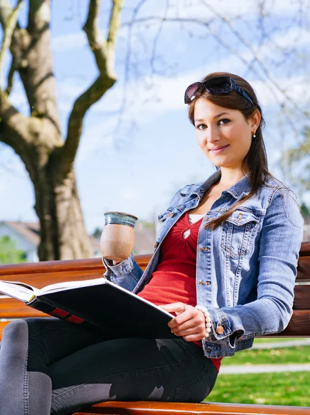 Beautiful woman drinking and reading on park bench — Stock Photo, Image