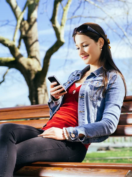 Beautiful woman using smartphone on park bench — Stock Photo, Image