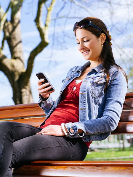 面带笑容的女人，在公园的长凳上使用智能手机 — Stockfoto