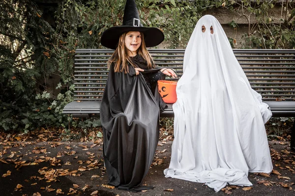 ベッドのシーツに身を包んだ若い男の子は幽霊 魔女の衣装を着た若い女の子はハロウィンのためにカボチャのペアを持っています — ストック写真
