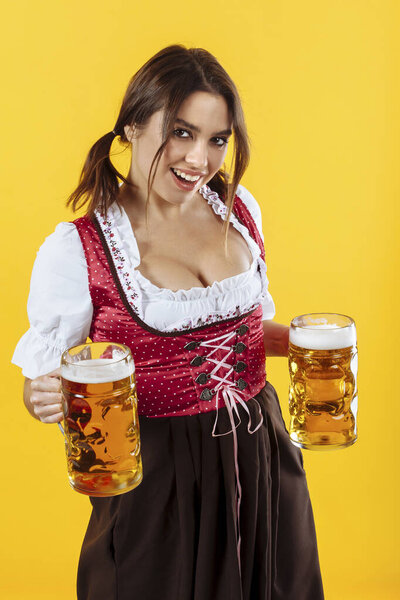 Красивая официантка в традиционной одежде и с двумя кружками пива на желтом фоне..