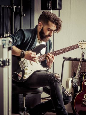 Sakallı ve elektro gitarını bir kayıt stüdyosunda çalan genç bir adam..