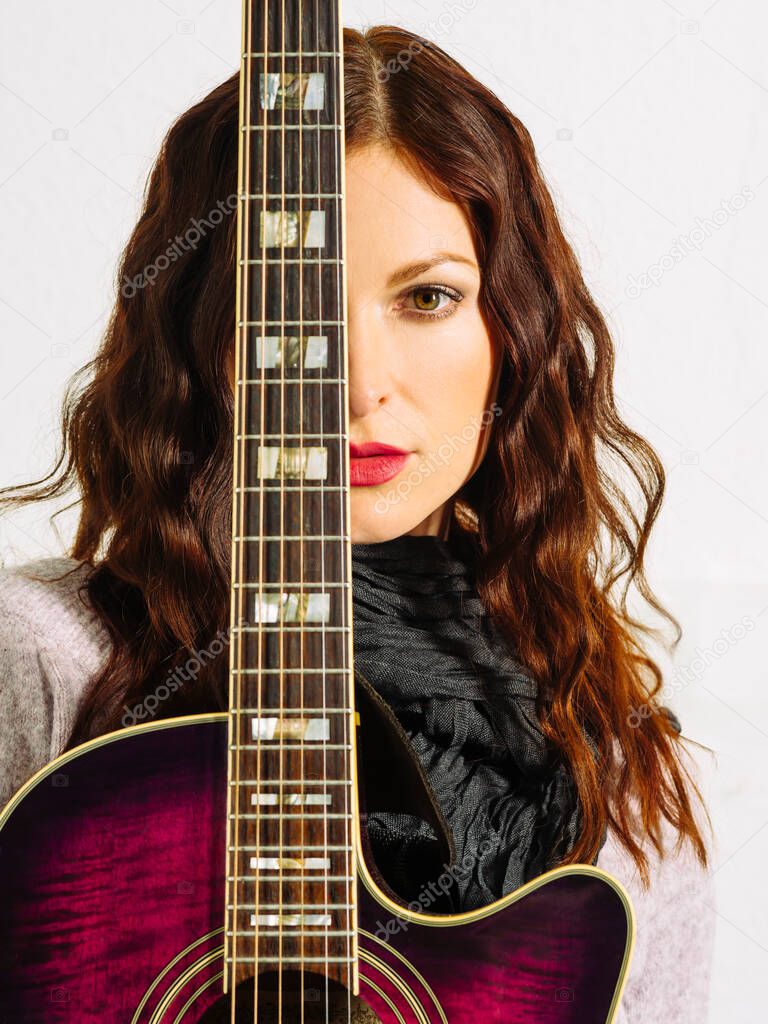 Young beautiful redhead woman holding an acoustic guitar over her face.