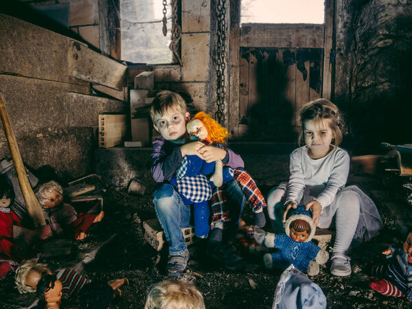 Creepy young children sitting with old dolls in a barn covered in spiderwebs and dust.