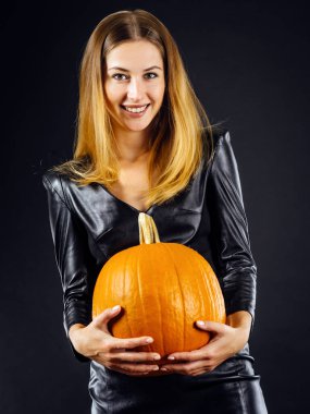 Young sexy woman in leather holding a pumpkin over smoky dark background for Halloween.