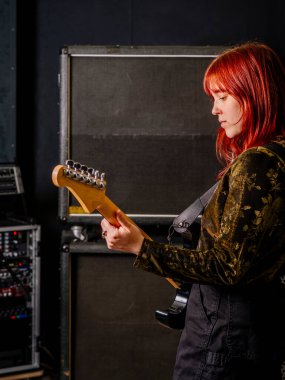 Genç kızıl saçlı kadın büyük hoparlörlerin önünde elektro gitar çalıyor..
