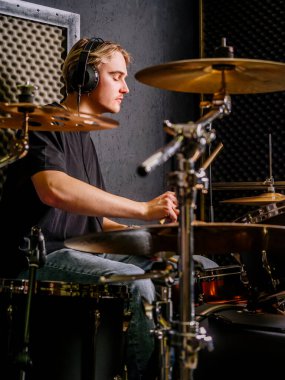 Genç adam kulaklık takıyor ve bir kayıt stüdyosunda davul çalıyor..