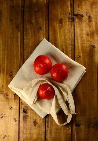 Fresh red tomatoes and bag on a wooden table — Stock Photo, Image