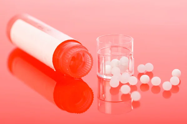 Pilules homéopathiques et récipient sur rouge — Photo