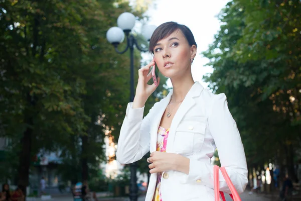 Krásné mladé ženy v bílém plášti mluví telefonu na ulici — Stock fotografie
