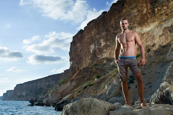 Homem de corpo perfeito com tronco nu em montanhas e fundo do mar. calças castanhas — Fotografia de Stock