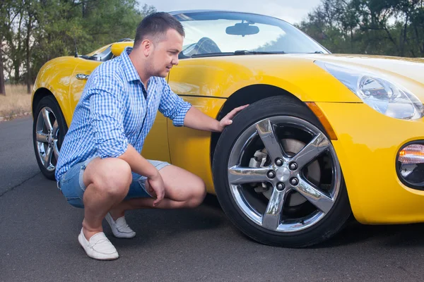 Young man cheeking tire of his convertible car — Stock Photo, Image