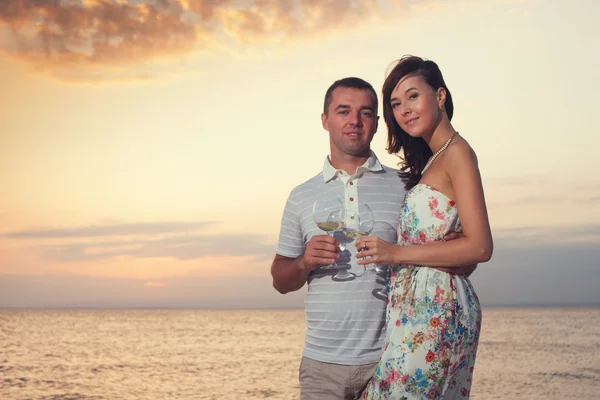 Casal sorridente segurando vinhedos durante o pôr do sol na praia do mar ou do oceano — Fotografia de Stock
