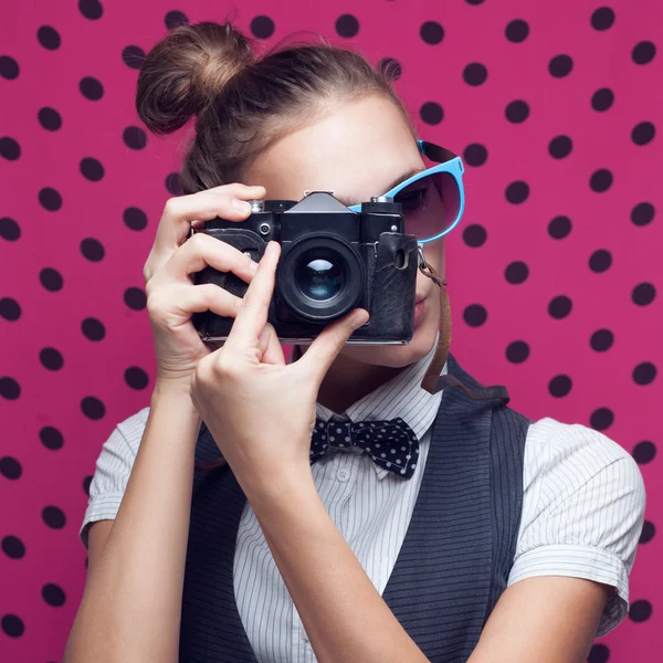 Portrait of beautiful hipster style young woman in white shirt and bow-tie. Old camera hanging by the neck — Stock Photo, Image