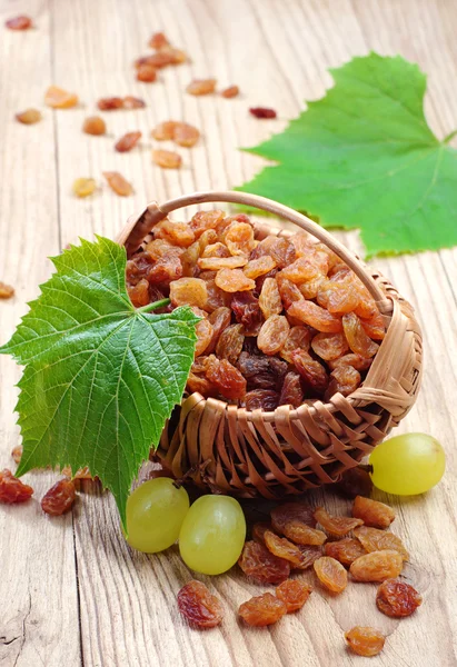 Rozijn in een rieten mand en druiven met bladeren — Stockfoto