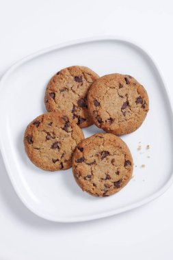 Beyaz arka planda bir tabakta çikolata parçacıklı kurabiyeler.