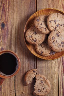 Çikolata parçalı kurabiyeler ve bir fincan kahve ahşap masada. Yakın çekim, üst manzara.