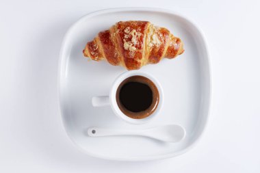 Taze pişmiş kruvasan ve beyaz arka planda bir tabakta bir fincan kahve.