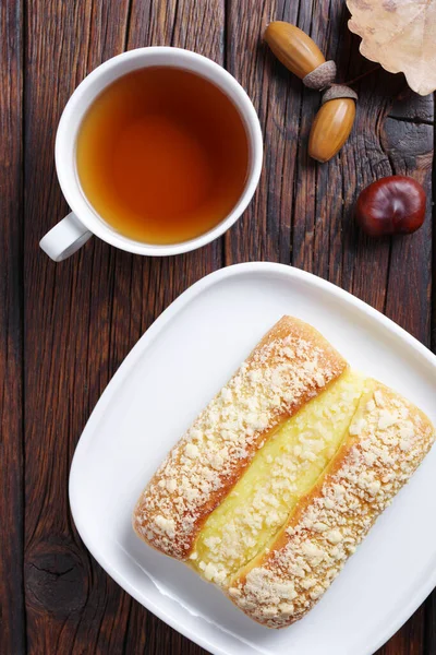 木の背景にクリームとお茶のカップと甘いパン トップビュー — ストック写真