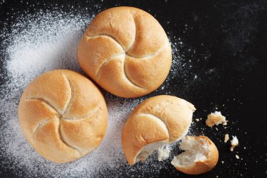 Siyah metal tepsinin arka planında küçük buğday ekmeği somunları, üst görünüm