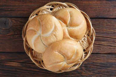 Hasır tabakta küçük buğday ekmeği, ahşap arka planda, üst manzara.