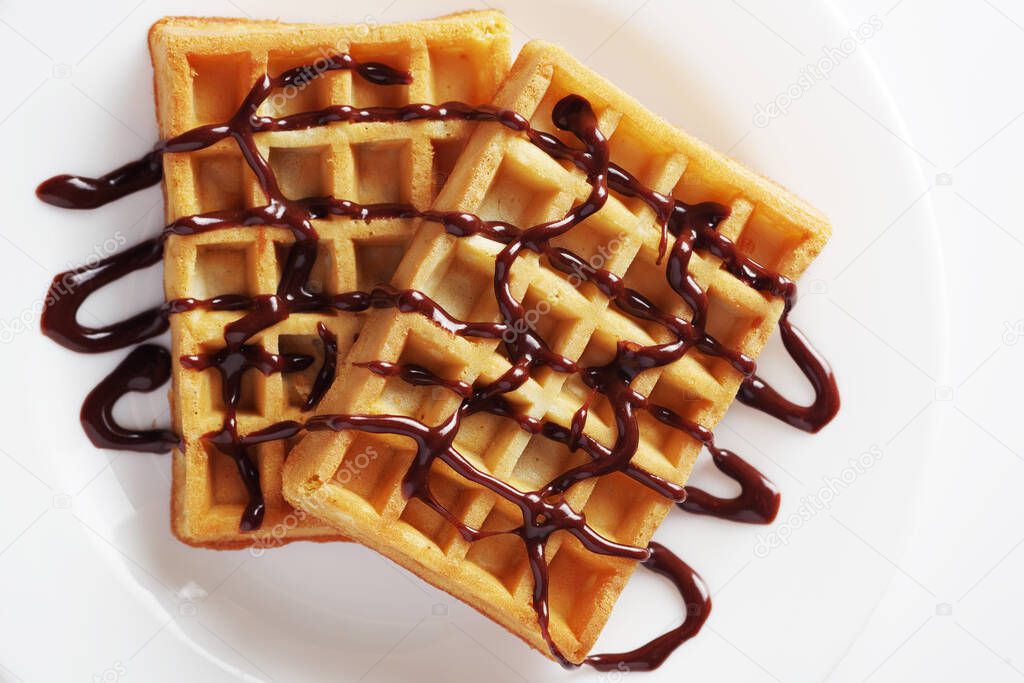 Stack of waffles with chocolate sauce on a plate on white background