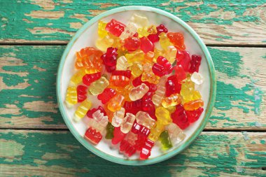 Eski yeşil ahşap arka planda, tabakta çok renkli jöle şeker ayıları, üst manzara