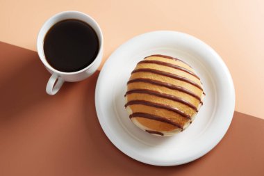 Çikolatalı çörek ve iki tonluk arka planda bir fincan kahve.